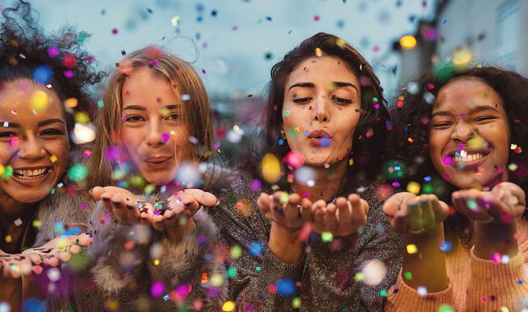 Article Cards Featured Image Young women blowing confetti from hands. Friends celebrating out