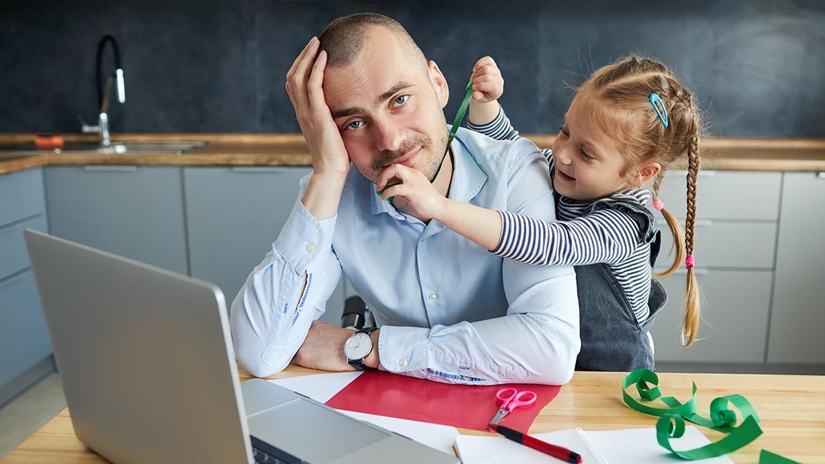 Article Cards Featured Image Father Working from home on laptop during quarantine. Little child girl make noise and distracts father from work on the kitchen office