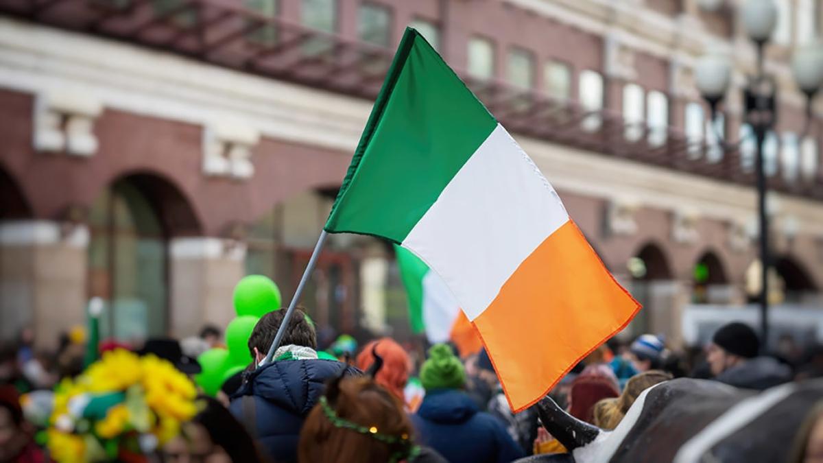 Article Cards Featured Image National Flag of Ireland close up in hands of man on background of crowd people in city street during celebration of St. Patrick's Day