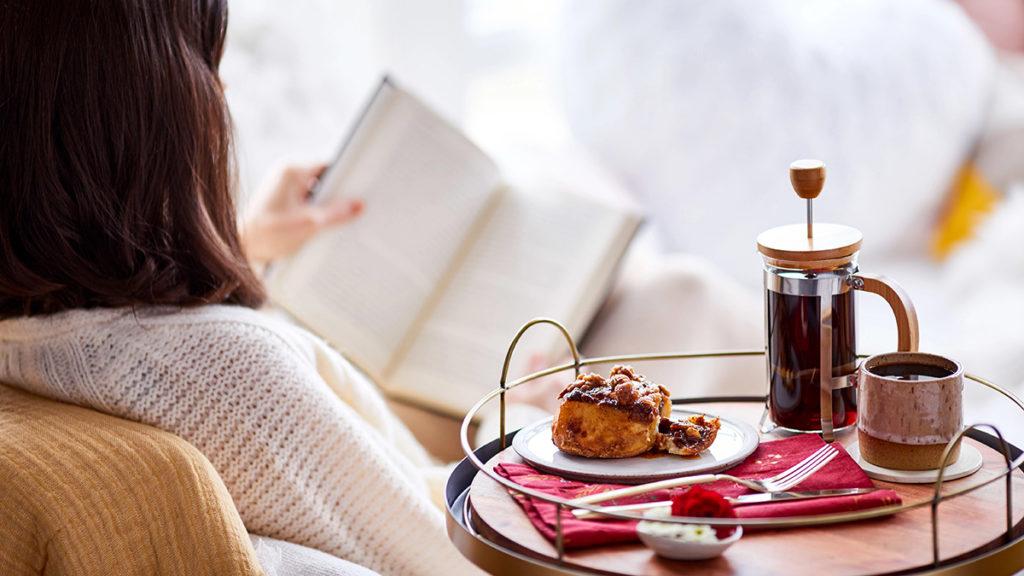 A photo of teacher gifts with someone sitting in a chair with their back to the camera next to a tray of coffee and baked goods