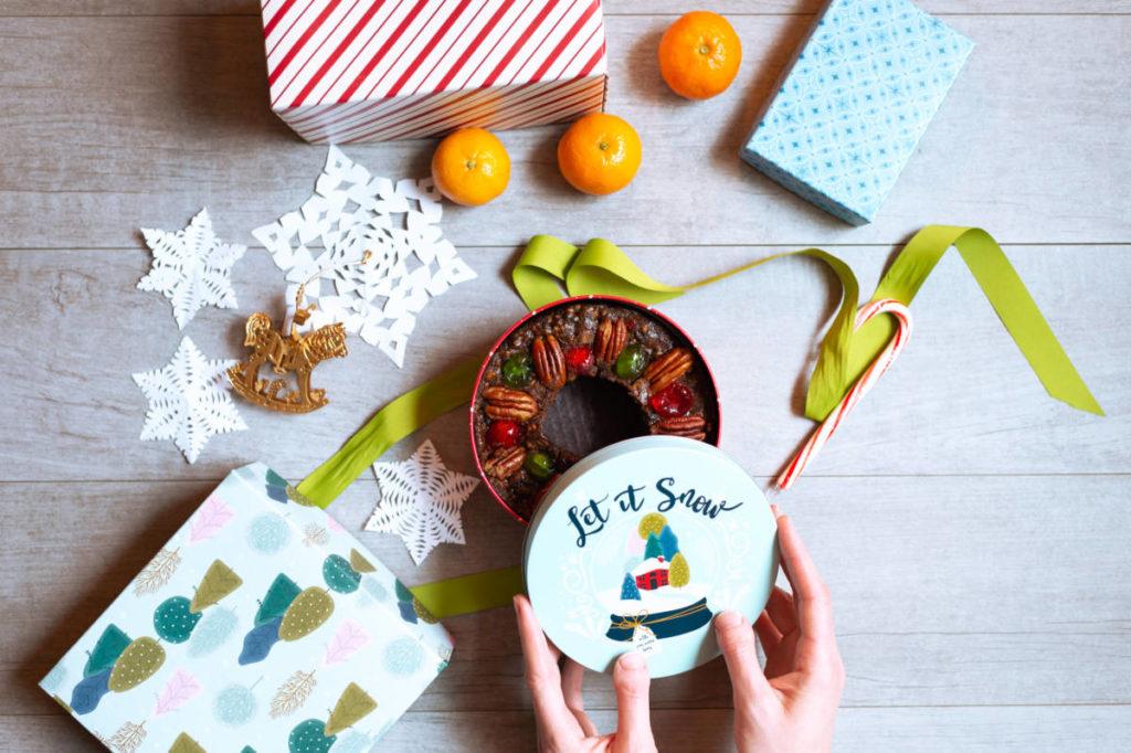 Fruitcake in a tin with a pair of hands lifting the lid off of it.