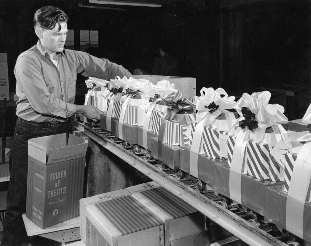 A photo of tower of treats with man packing stacks of decorated boxes.