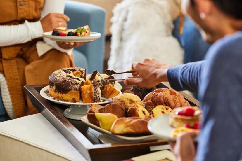 A photo of winter gifts with a tray of baked goods and three people sitting around it while one person serves themselves a slice of cake.