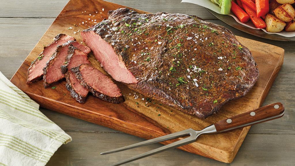 A photo of Passover wine with a cooked brisket on a wooden cutting table with a few slices of brisket next to it.