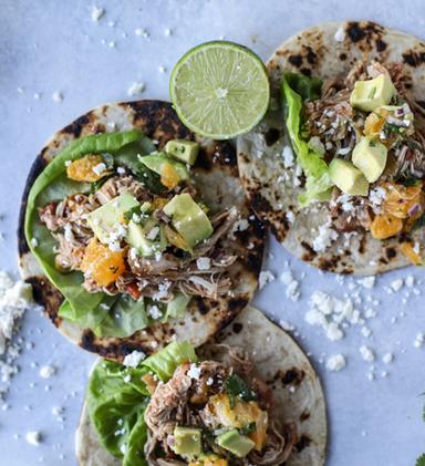 Photo of how to ripen an avocado with three open chicken tacos on a table.