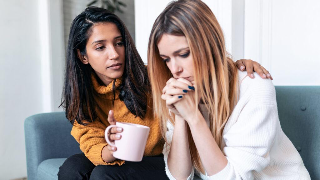 Comfort food with a woman comforting another woman while sitting on a couch.