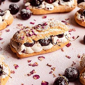 Several cherry eclairs on a pink counter top.