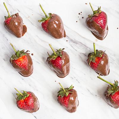 Rows of chocolate covered strawberries on a marble counter.